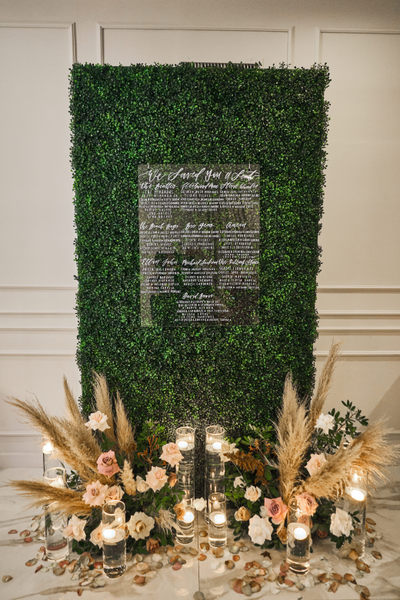 Green grass rectangular panel backdrop with clear acyrlic sign on it with lettering on it. Boho flower arrangments are on both corners of the panel. 