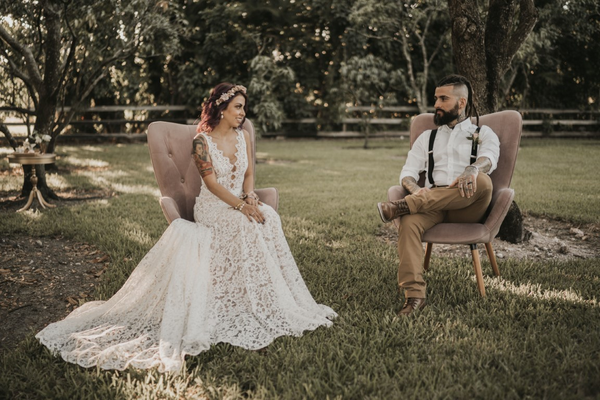 Modern vintage dusty pink pastel tufted velvet chairs with a couple sitting on each one outdoors on the grass. 