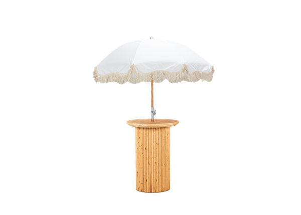 light wood cocktail table with a textured base paired with a white fringe umbrella 