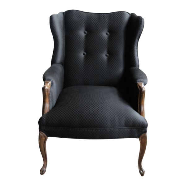 Black tufted wingback chair with dark wood accents