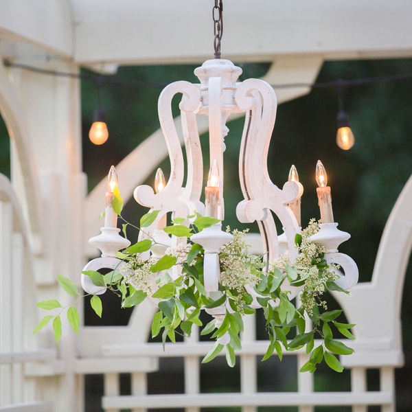 Wood French style chandelier with green smilax and flowers hanging in arbor for wedding reception.