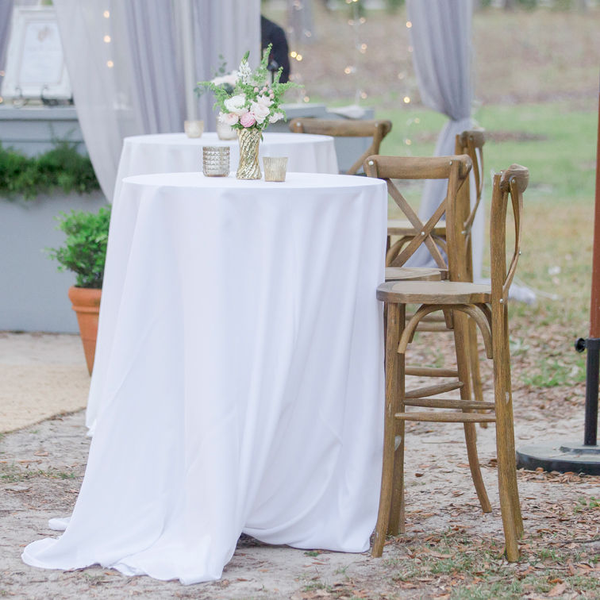 Wood bar stools at outdoor wedding reception with white tablecloths and white flowers.