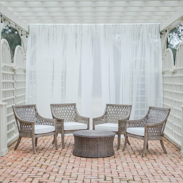 Wicker coffee table surrounded by rattan wicker chairs with draping sheers at The Space at Feather Oaks.