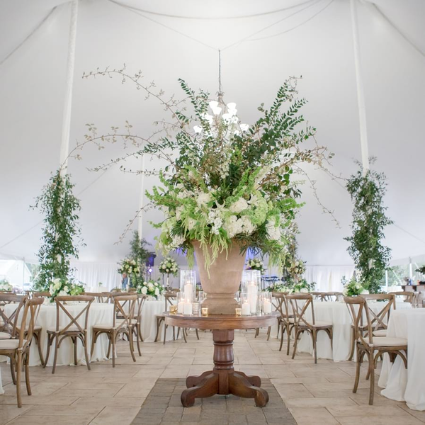 Large wedding urn with white hydrangea on top of wood table under tent with farm chairs.
