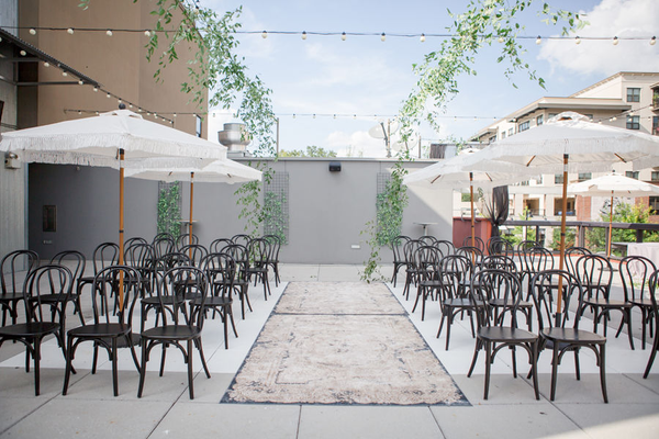 Smilax hanging over boho black wedding chairs and white patio umbrellas for Madison Social rooftop wedding.