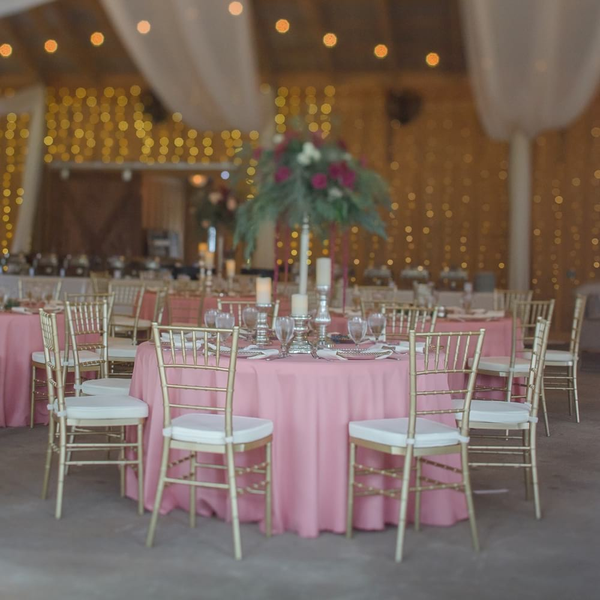 Round tables with pink linens and gold Chiavari chairs inside barn at Loblolly.