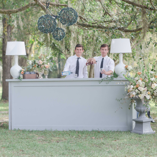 Bartenders pouring drinks with grey bar and white lamps for outdoor wedding reception.