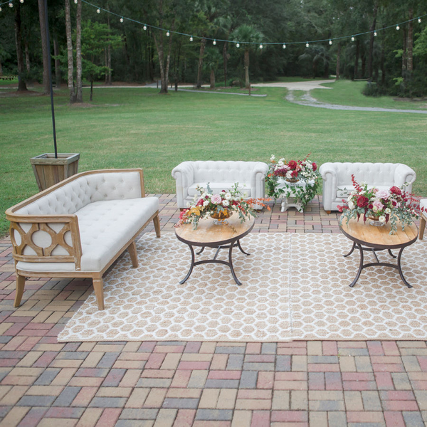 Outdoor wedding lounge vignette with wood oval tables and sofa and honeycomb rug at Lewis Wood Farms.