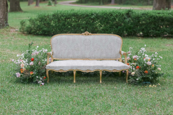 French style wedding settee surrounded with flowers and boxwood hedge.