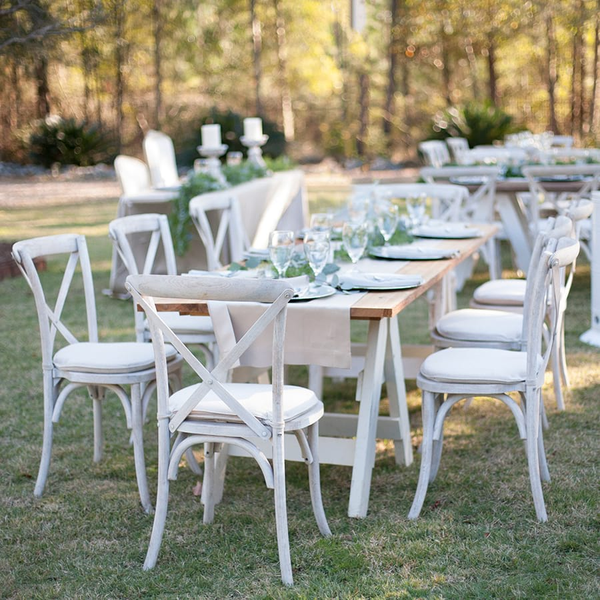 White farm cross back chairs with farm tables setup for outdoor wedding reception.