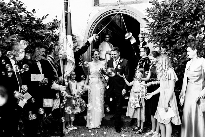 Braut und Bräutigam schreiten durch den historischen Torbogen von Schloss Neuhaus bei Sinsheim, umgeben von eleganten Mauern und strahlenden Gästen.