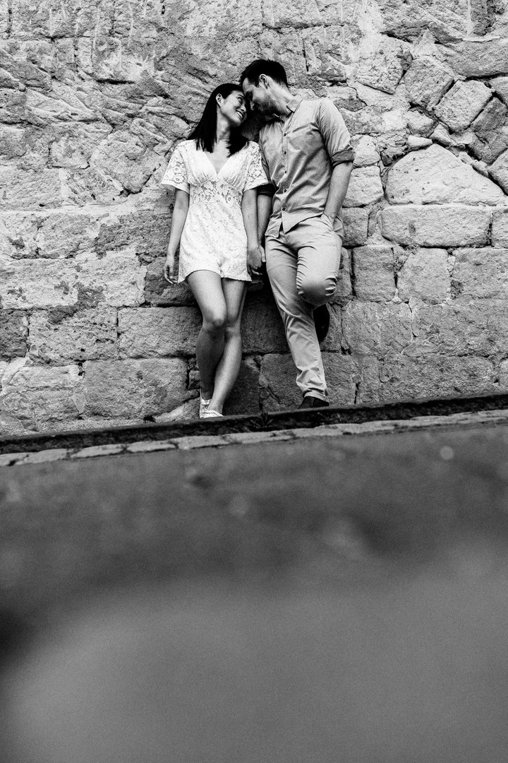 Nahaufnahme des Paares vor der rustikalen Sandsteinmauer in Tübingen: Sie berühren sich sanft mit den Köpfen, während ihr Blick zärtlich ineinander versinkt.