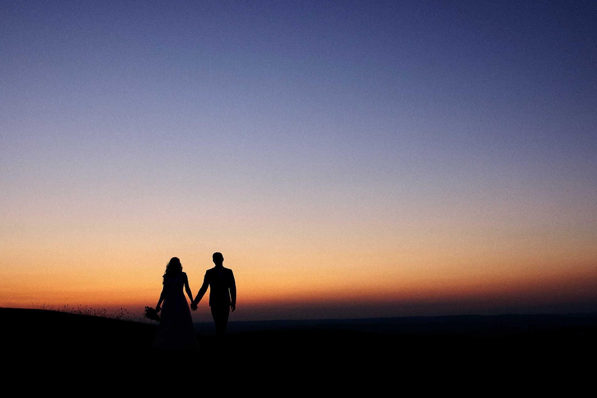 Silhouette eines Brautpaares bei Sonnenuntergang, Hand in Hand, symbolisiert romantische Hochzeitsmomente.