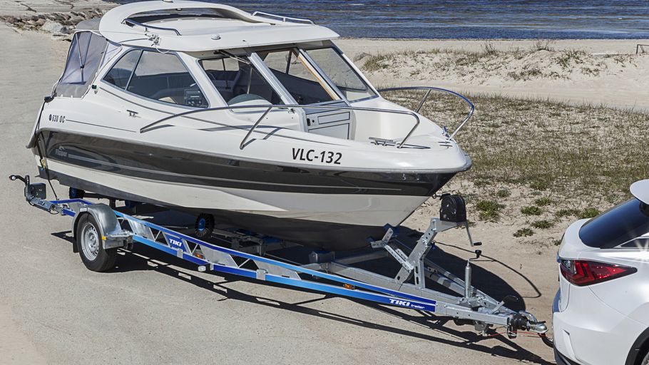 Mindre båt på båtrailer bakom personbil vid strand