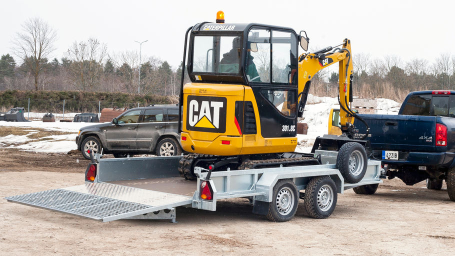 Bil med maskintrailer lastad med minigrävare