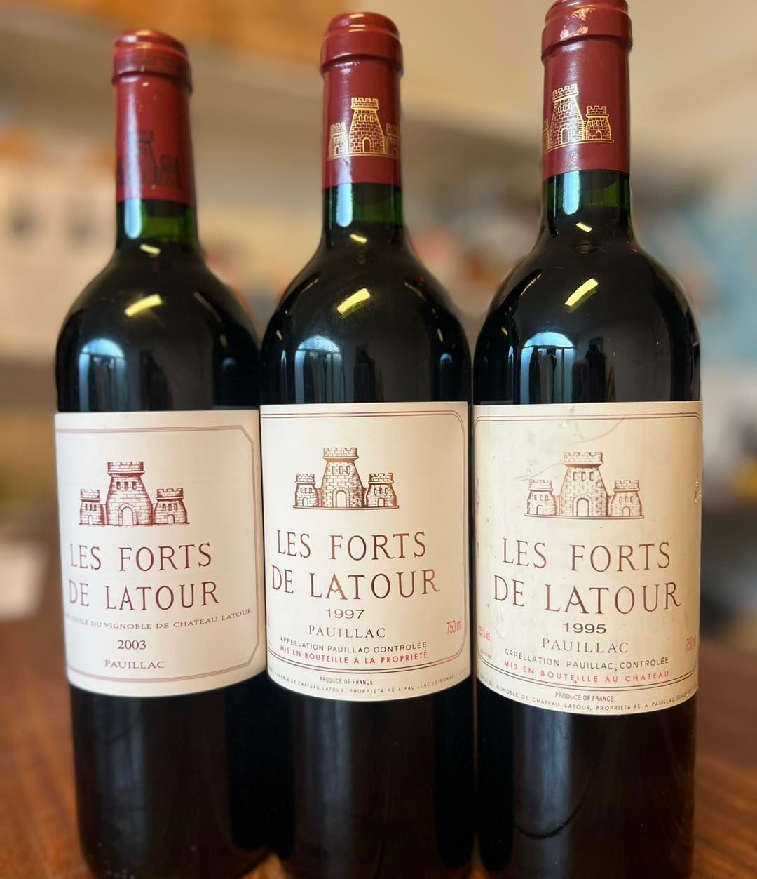 三支直立酒瓶,酒標年份是 2003、1997 和 1995,都印有 LES FORTS DE LATOUR 和 PAUILLAC,紋章是塔樓