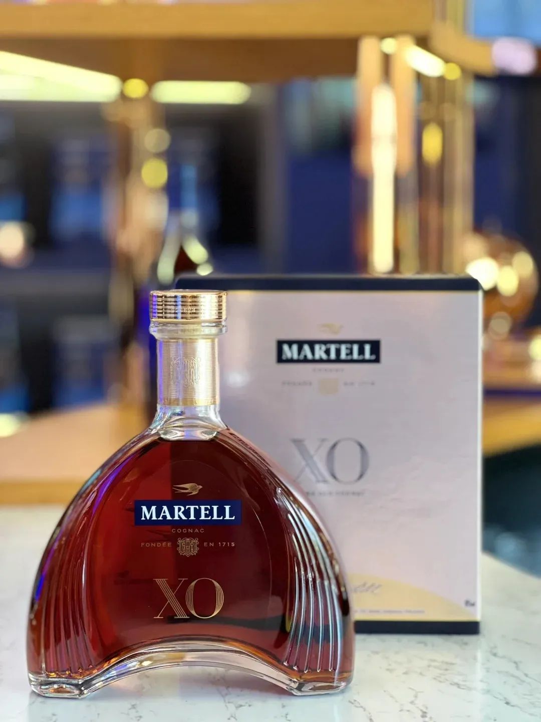 弧形 Martell XO 酒瓶置於淺色 XO 外盒前，瓶身及盒面均可見 XO 字樣