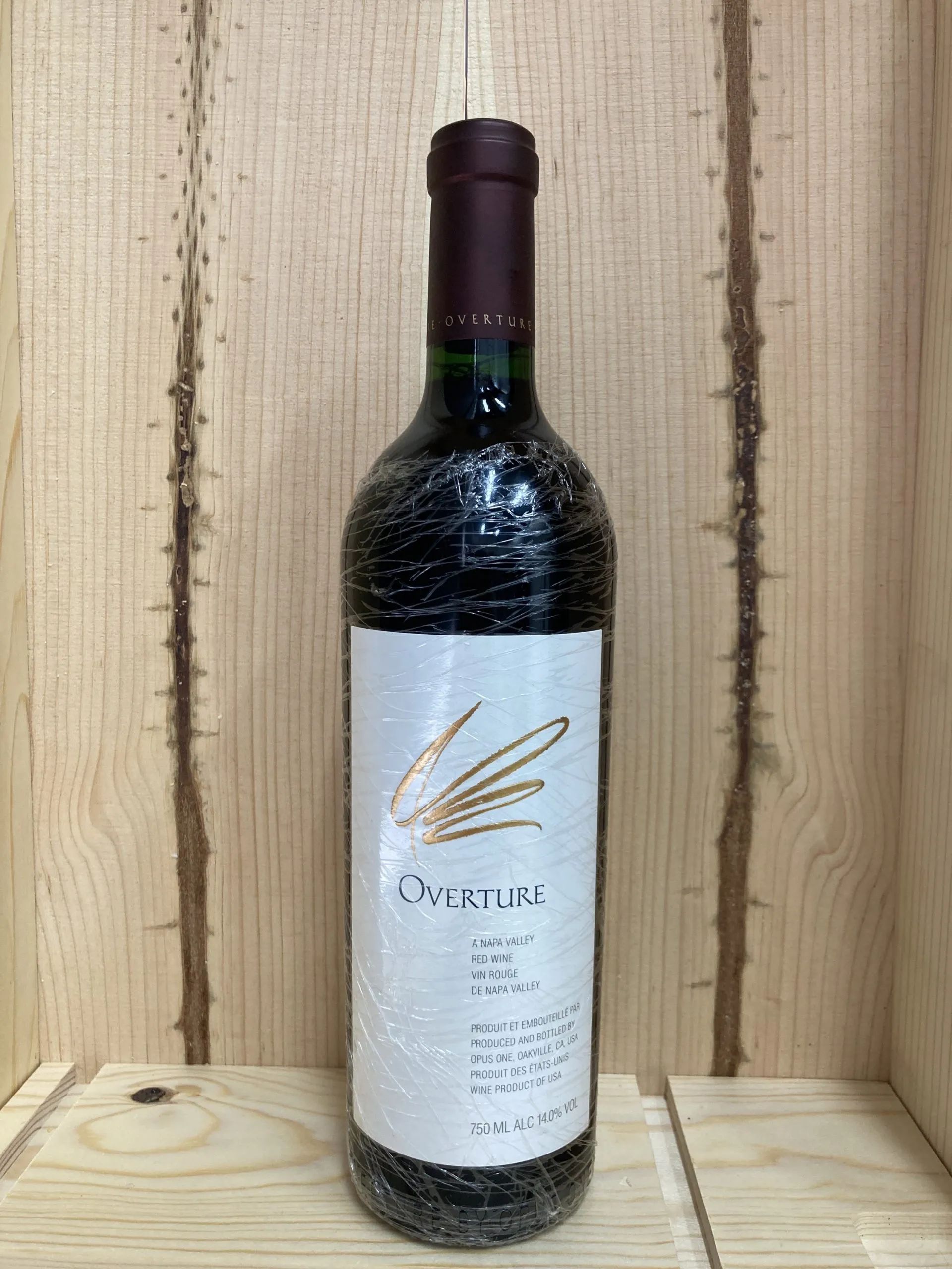 一支酒瓶直立在淺色木箱內,栗色瓶帽印有 OVERTURE,酒標寫 OVERTURE 與 A NAPA VALLEY RED WINE,並註明由 Opus One 生產