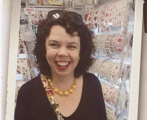 Smiling woman with curly dark hair and a yellow beaded necklace in a craft store
