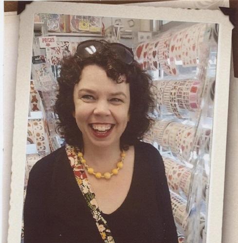 Smiling woman with curly dark hair and a yellow beaded necklace in a craft store