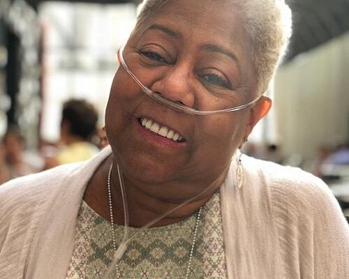 Older woman with short gray hair smiling while wearing a nasal cannula
