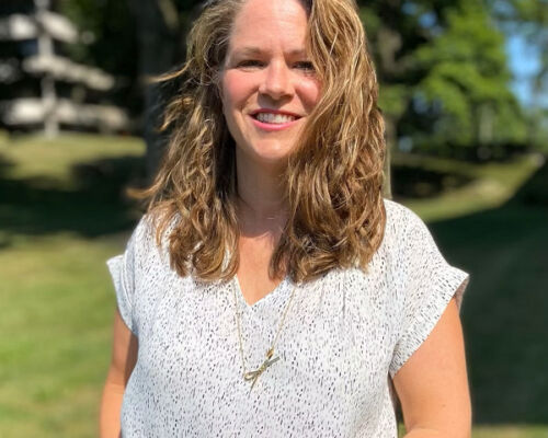 Help Hope Live Director of Outreach Sonny Mullen is outside of a corporate office. She has light skin, curly light brown hair to her shoulders, and a white blouse.