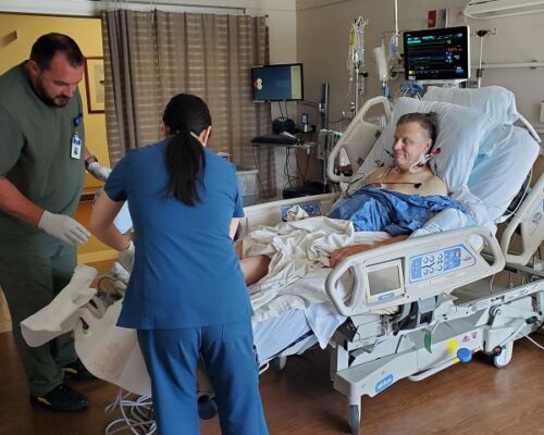 Two healthcare workers attend to a smiling patient in a hospital bed connected to medical monitors