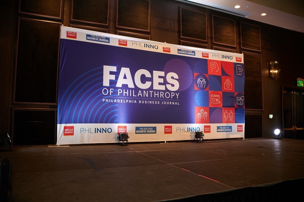 An extra-large banner on stage reads Faces of Philanthropy: Philadelphia Business Journal with dark blue, purple, white, and orange graphical accents.