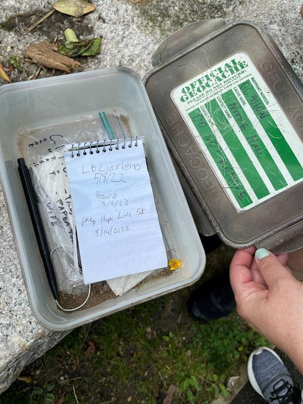 A geocaching station with a handwritten white note covering other assorted items.