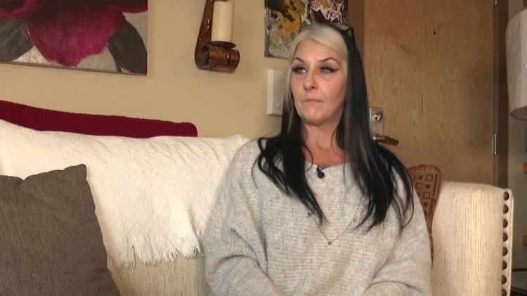 Kidney transplant candidate Jeannie Jerri Lewis sits on her couch. She has light skin, blonde and black dyed hair, wing-tipped mascara, and green eyes.