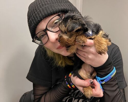 Person in a black beanie and glasses holding a small brown-and-black dog