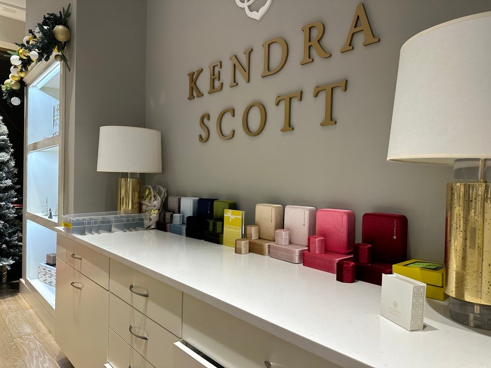 A photo of a Kendra Scott counter with the Kendra Scott name in gold and eight packaging sets for jewelry in jewel tones.