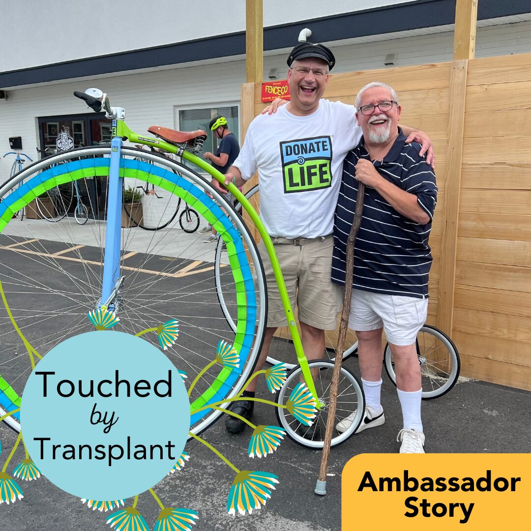 A photo of heart transplant recipient Bill Soloway and his heart donor's father next to Bill's highwheel bicycle. Bill has light skin and gray hair with glasses and wears a Donate Life t-shirt and shorts. His donor's father has light skin, white hair, glasses, and shorts. His high wheel bicycle is decked out in Donate Life blue and green.