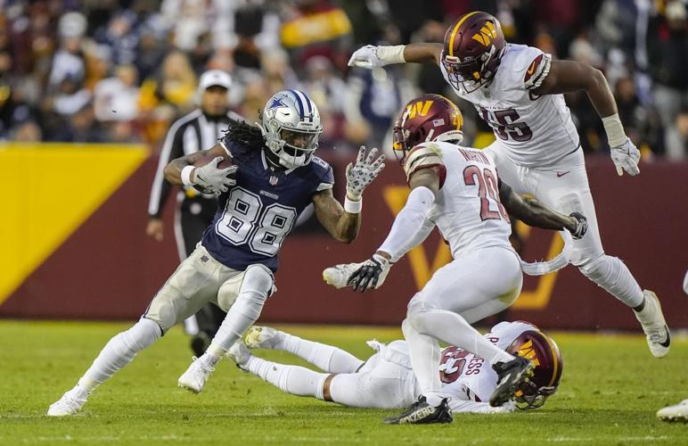 An action shot of KJ Henry and his teammates on the field of an NFL game. KJ plays for the Washington Commanders and he and his teammates are wearing Commanders uniforms in signature white, maroon, and gold on the bright green field.