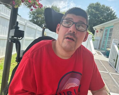 Man wearing glasses and a red shirt seated in a wheelchair outdoors