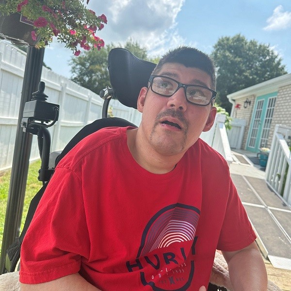 Man wearing glasses and a red shirt seated in a wheelchair outdoors
