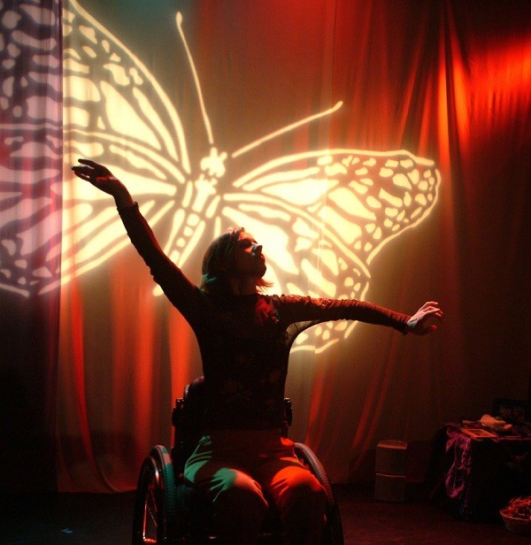 A person in a wheelchair poses with arms outstretched in front of a large projected butterfly