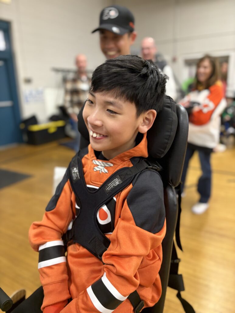 13-year-old Max Peng in Flyers orange receiving his customized adaptive bike.