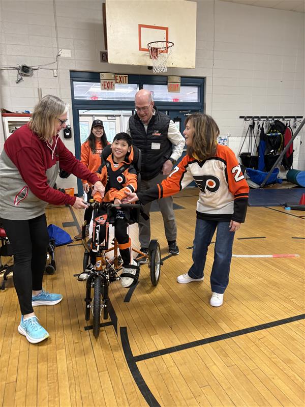 13-year-old Max Peng in Flyers orange receiving his customized adaptive bike from Brad Marsh.
