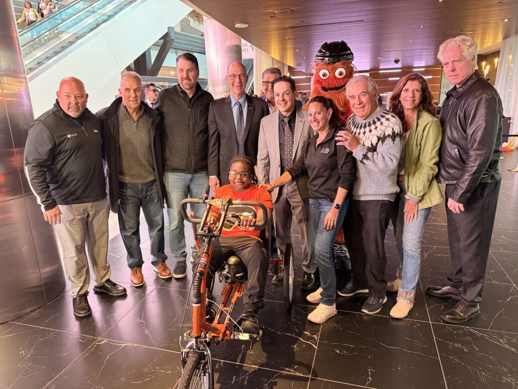 Raymeer riding his adaptive bike with Help Hope Live staff and Flyers Alumni in October 2025