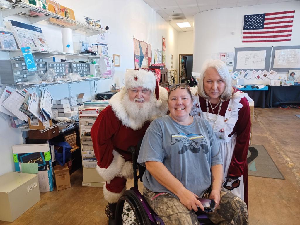 Help Hope Live client Jamie Carlson aka the "Cerebral Palsy Quilter" in her power chair with Mrs. Claus and Santa Claus.