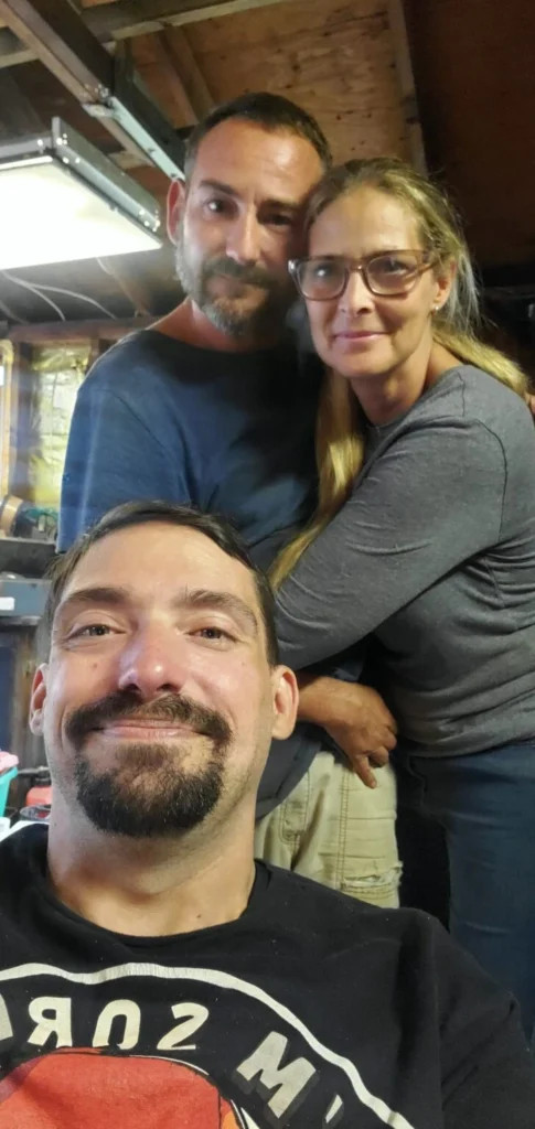 Selfie with Scott Hughes seated in his chair and 2 people standing behind him.