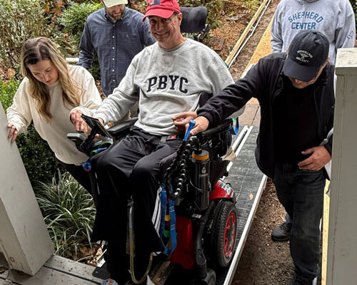 Wheelchair user assisted up an accessibility ramp by friends and family