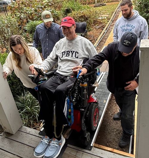 Wheelchair user assisted up an accessibility ramp by friends and family