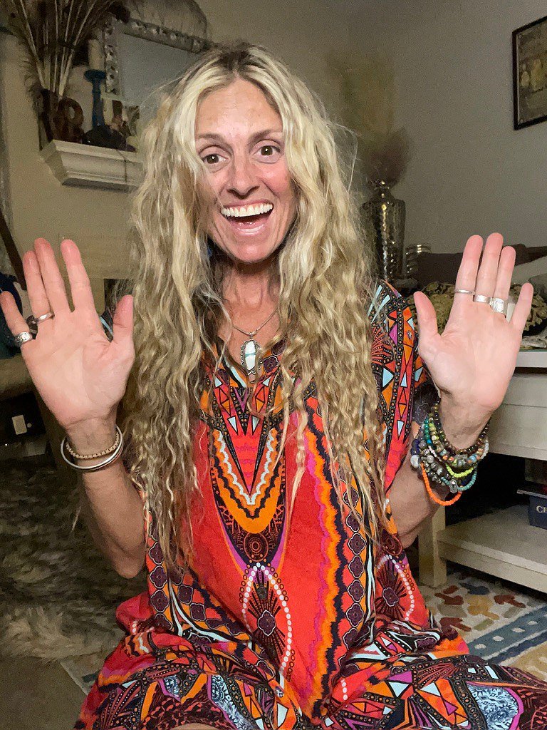 Noelle Doughty smiling with both hands raised, wearing a colorful patterned outfit