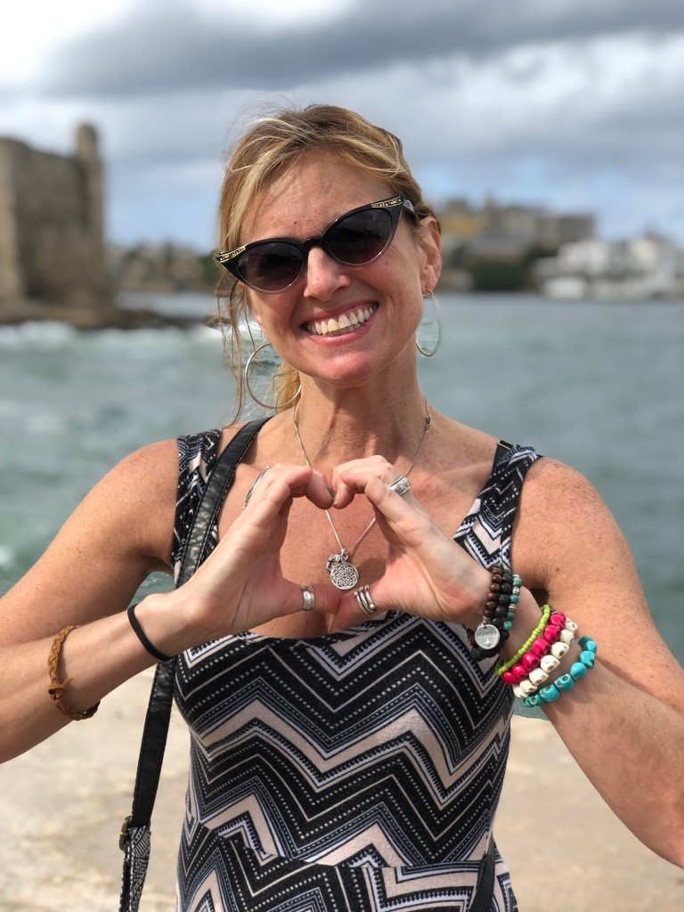 Noelle Doughty smiles and forms a heart with her hands near the waterfront