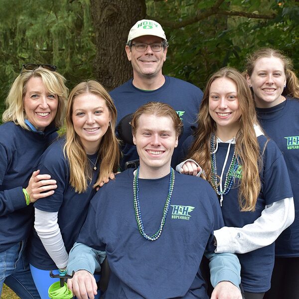 Six smiling people wearing matching navy shirts pose together outdoors among trees