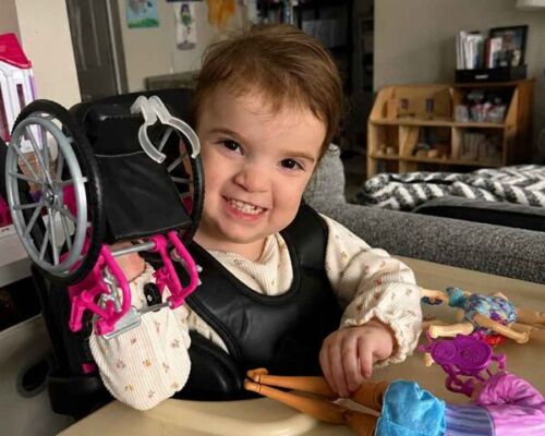 Smiling child seated in a wheelchair at a table with colorful toys