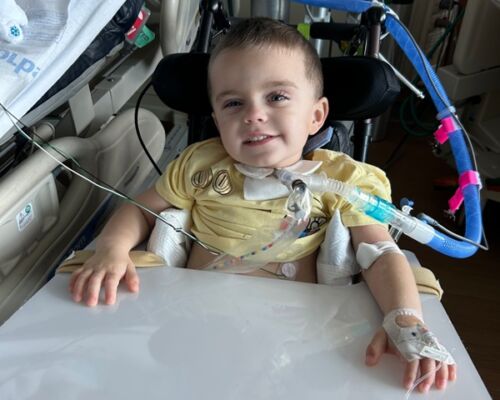 Child smiling in a hospital bed, connected to medical tubing and equipment
