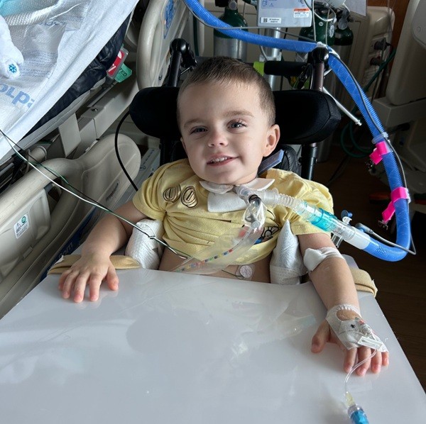 Child smiling in a hospital bed, connected to medical tubing and equipment